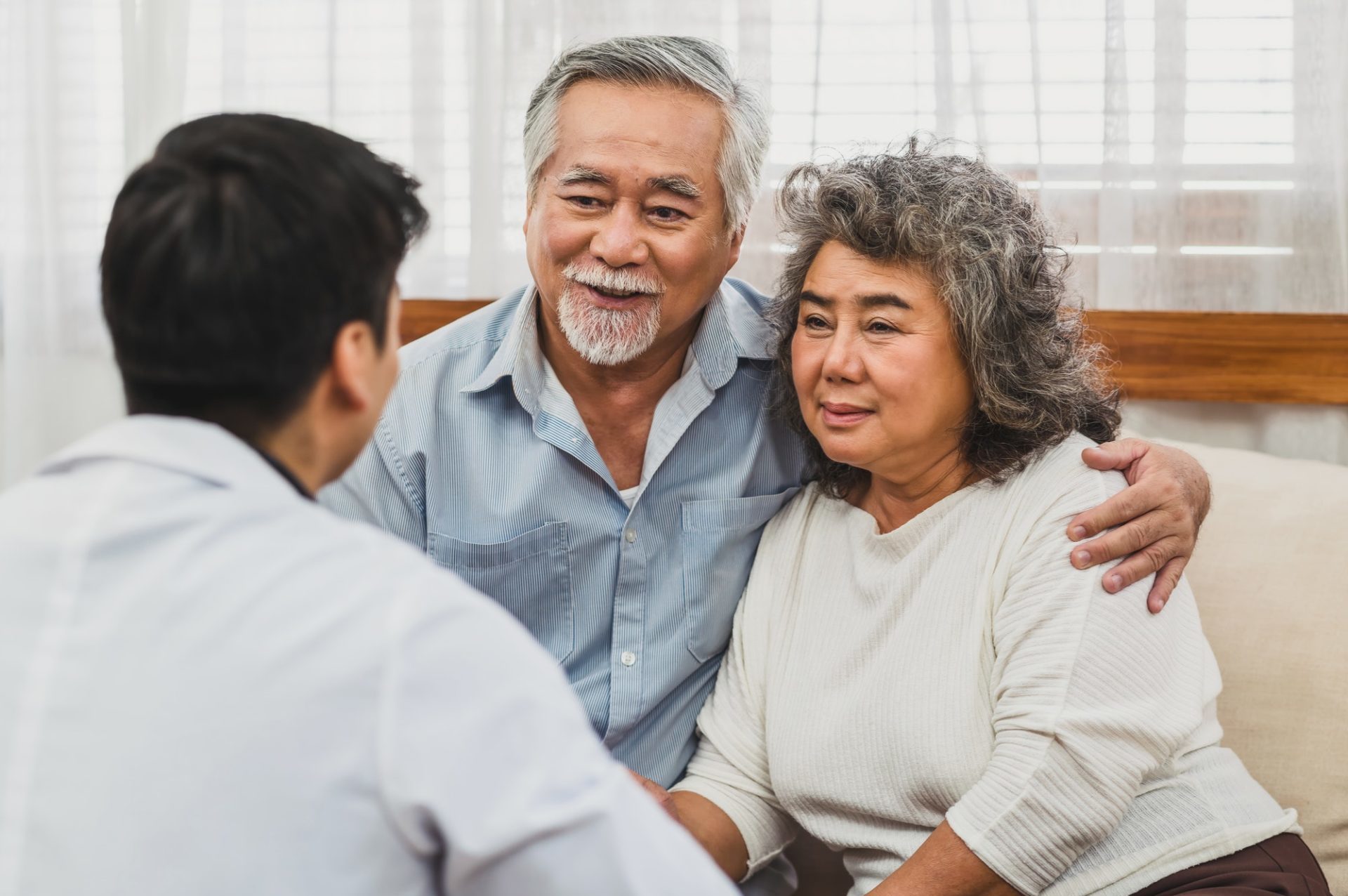 rear-view-of-doctor-give-advice-to-couple-asian-grandparent-patient-in-house-service-life-insurance-e1658385240540.jpg